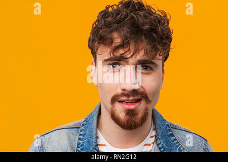 Nahaufnahme eines verwirrten jungen bärtigen Mann leger gekleidet stehen über orange isoliert Stockfoto