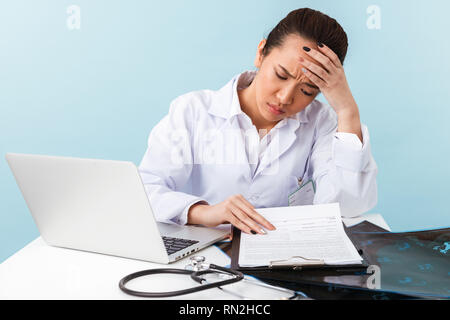 Foto eines Jungen müde Langeweile Frau Doktor mit Kopfschmerzen über blaue Wand mit Laptop Computer Hintergrund posiert. Stockfoto