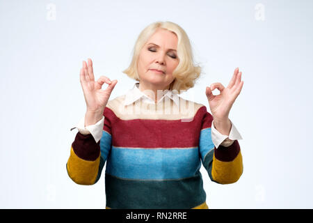 Entspannt senior Frau genießt eine ruhige Atmosphäre, hält die Hände in mudra Zeichen Stockfoto