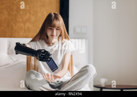 Am ersten Tag mit einer prothetischen Arm. schließen Foto. behinderte Mädchen entfernt das Telefon von einer Hand in die andere. nach oben schließen Foto Stockfoto