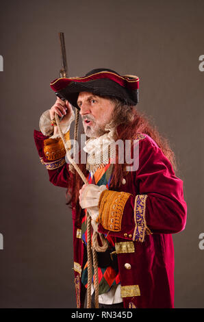 Alte meer Hund, Piraten Kapitän mit Muskete, holding Seil in den Händen, Studio shot vor grauem Hintergrund Stockfoto