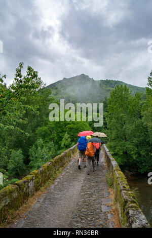 Conques, Frankreich - Juni 2015: eine Gruppe von Pilgern überquert einen kleinen Fluss auf einem Stein Brücke entlang der Hl. Jakobus Pilgerweg in Conques Stockfoto