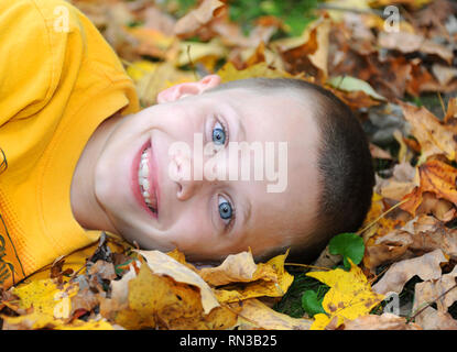 Little boy Balken einem Lächeln, als er im Herbst Blätter im östlichen Tennessee spielt. Er ist zur Festlegung der mit dem Kopf auf den gelb-goldenen Blätter. Stockfoto