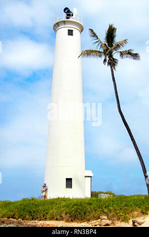 Paar steht an der Basis der Friseur's Point Lighthouse Vergleich der Größe zu zeigen. Einsame Palme lehnt sich in Richtung Leuchtturm, der auf Oahu in Ha steht Stockfoto