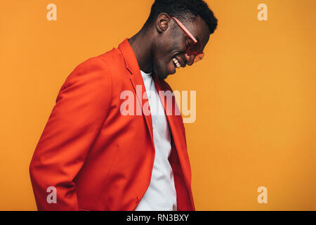 Schöne afrikanische Mann Mode Modell mit Sonnenbrille lächelnd gegen orange hinterlegt. Stilvolle afrikanischer Mann lächelnd im Studio. Stockfoto