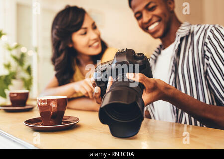 Junge Mann zeigt Bilder auf seine DSLR-Kamera zu seiner Freundin im Cafe. Mann seine neue Inhalte zeigen, Weibchen auf der Digitalkamera im Cafe. Stockfoto