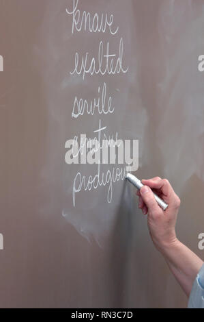 Lehrer schreibt Liste von Wörtern auf einer Tafel. Sie hält ein Stück Kreide. Stockfoto