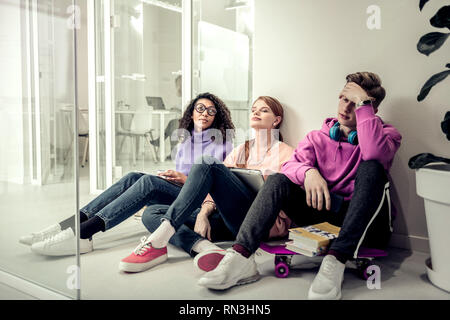Blonde Schüler sitzen in der Nähe seiner Freunde Müdigkeit und Langeweile Stockfoto