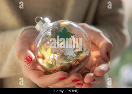 Hände von Frau mit Weihnachtskugel mit Stern Konfetti Stockfoto