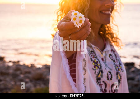 Fröhliches happy freee kaukasischen mittleren Alter Frau in hippy Fashion Kleidung nehmen eine schöne daisy flower - Fokus auf Blumen und sun Hintergrundbeleuchtung - Sonnenuntergang i Stockfoto
