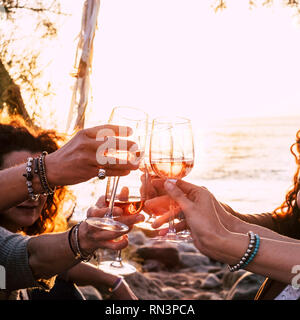Die Leute trinken bei Party outdoor. Gruppe von Freunden weiss Wein in der Hand Toasten mit Brille. Bis auf Hände und Getränke in der Nähe - landschaftlich schöne Sonnenuntergang ein Stockfoto