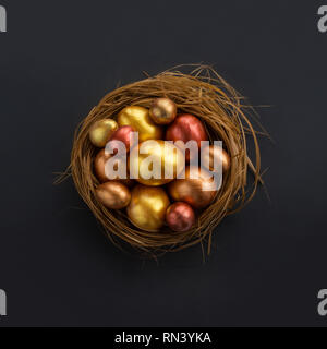 Frohe Ostern Urlaub gruss Symbol stilvollen natürlichen Holz- Gras Nest mit goldenen Wachteleier auf schwarzem Hintergrund Stockfoto