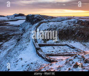 Morgendämmerung erhebt sich über Milecastle 39, Highshied Felsen und Crag Lough auf Hadrian's Wall, im Winter mit Schnee bedeckt, in Northumberland. Stockfoto