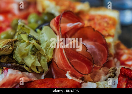 Antipasti Teller mit Wurstwaren wie Schinken, Salami, Soppressata, Bresaola und Porchetta, Gemüse wie Artischockenherzen, Oliven, Peperoncini Stockfoto