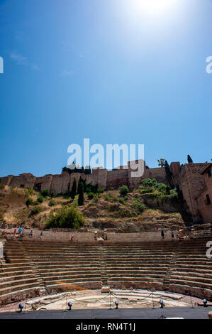 Touristen, die sich in der römischen Amphitheater mit der maurischen Festung oder Alcazaba im Hintergrund, Malaga, Spanien. Stockfoto