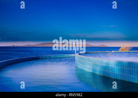 Blautöne, bei denen das künstliche Blau des Pools auf das tiefblaue Meer und den Himmel trifft. Stockfoto