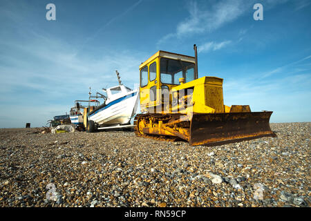 Alten gelben Bulldozer abschleppen ein kleines Fischerboot auf einem Kieselstrand Stockfoto