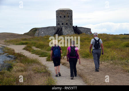 Drei Wanderer zu Fuß bis zu den Loopholed Martello Rousse Turm Nr. 11 mit Blick auf den Le Grand Havre Bay auf dem Küstenweg, Guernsey, Channel Islands.de. Stockfoto