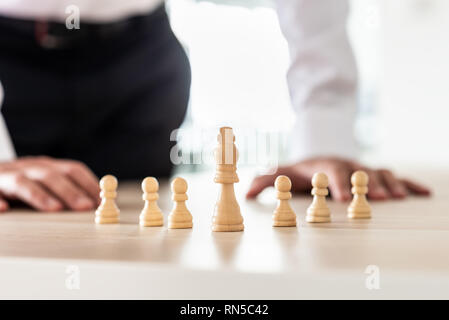 Schachfiguren König und Bauern auf Büro Schreibtisch platziert mit King als Marktführer und Geschäftsmann im Hintergrund in einem konzeptionellen Bild. Stockfoto