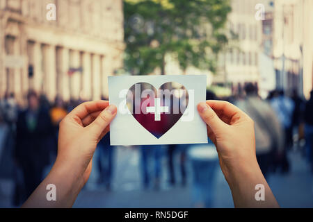 Gesundheit und Wohlbefinden globales Problem als menschliche Hände halten ein Blatt Papier mit Herz und Kreuz Symbol auf einer belebten Straße Hintergrund. Healthcare Medical Stockfoto