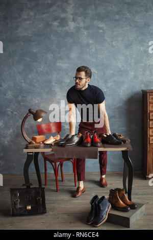 Schuhdesigner bieten seine Schuhe zu Kunden, volle Länge Foto. Jake Alleskönner, blaue Wand auf dem Hintergrund der Foto Stockfoto