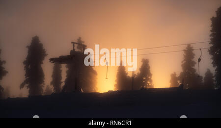 Silhouette von Skilift und Bäume im Winter gegen Golden Sunset mit Sonnenstrahlen durch Nebel im Skiort Levi in Kittilä, Finnland Stockfoto