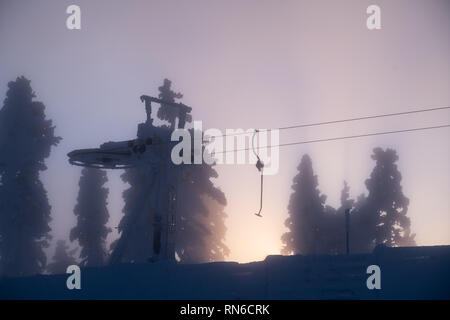 Silhouette von Skilift und Bäume im Winter mit Sonnenstrahlen durch Nebel im Skiort Levi in Kittilä, Finnland Stockfoto