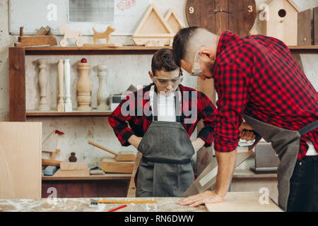 Vater und Sohn Arbeiten in der Werkstatt. Sie sind Sägen Holzbohlen. Stockfoto