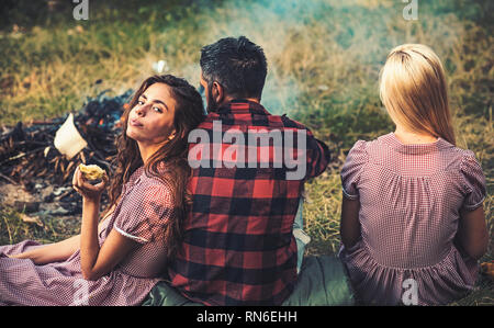 Brunette Mädchen lehnte sich auf ihren Freund. Drehen Sie wieder Freunde sitzen auf Gras neben dem Lagerfeuer. Romantisches Wochenende in der Natur Stockfoto