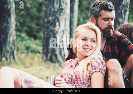 Blonde Mädchen lehnte sich auf ihren Freund. Gruppe von Freunden sitzen im Gras neben dem Lagerfeuer. Romantisches Wochenende in der Natur Stockfoto