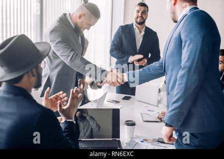 Geschäftsleute, die in förmlichen tragen die Hände schütteln, bis Beendigung einer Versammlung, der Einführung multiethnischer Partnerschaft, zu beschäftigen. Stockfoto