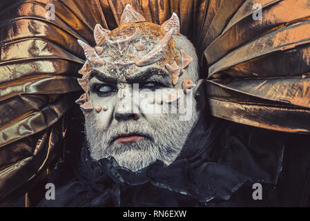 Mann mit Stacheln oder Warzen, Gesicht mit glitzert abgedeckt. Dämon mit goldenen Kragen auf schwarzem Hintergrund. Alien, Dämon, Zauberer Make-up. Fantasy Konzept Stockfoto