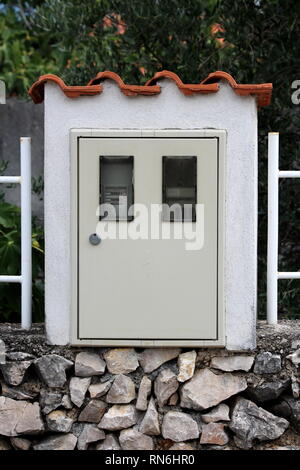 Stromzähler auf traditionellen Steinmauer in konkreten Rahmen mit einem Meter und Sicherheitsschalter innen sichtbar durch kleine Fenster montiert Stockfoto