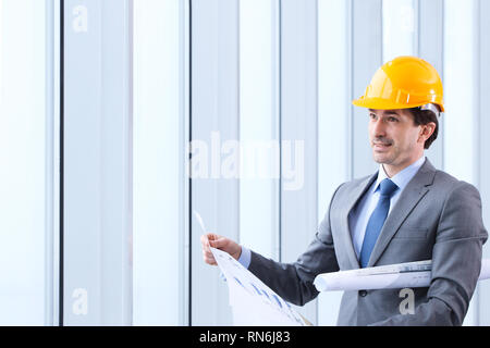 Architektur, Bau und Gebäude - Lächeln, Architekt oder Unternehmer in Gelb hardhat und Anzug mit Blueprint durch das Fenster Stockfoto