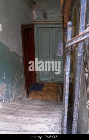Abgenutzte hölzerne Treppe, die zu grünen und roten Türen Stockfoto