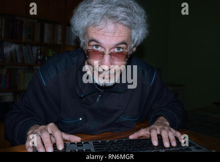 Porträt der grauhaarige Mann mit einer Tastatur vor computer monitor Stockfoto
