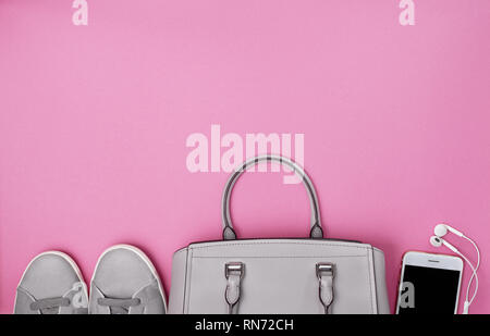 Damen Handtasche, grau Sneakers, ein Smartphone mit Kopfhörern auf einem rosa Hintergrund. Blick von oben. Kopieren Sie Platz Stockfoto