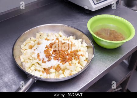 Fresh Cut Apfel Würfel, bestreut mit Zucker, Rosinen in Schale mit Wasser, für die Herstellung von apple charlotte Pie auf dem Restaurant Küche. Konzept confectione Stockfoto