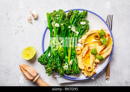 Gekochte broccolini mit Hummus auf eine weiße Platte, Ansicht von oben. Gesunde vegane Ernährung Konzept. Stockfoto
