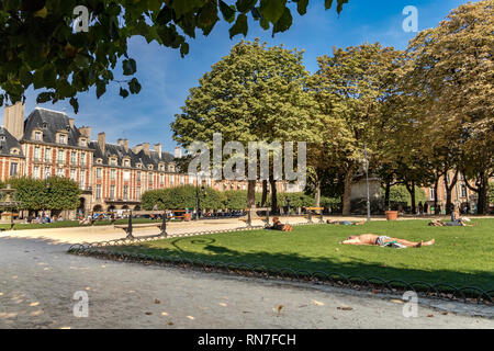 Menschen sitzen und sonnen sich auf dem Rasen in der Nähe des Brunnens am Place des Vosges , im schicken Viertel Le Marais in Paris, Frankreich Stockfoto