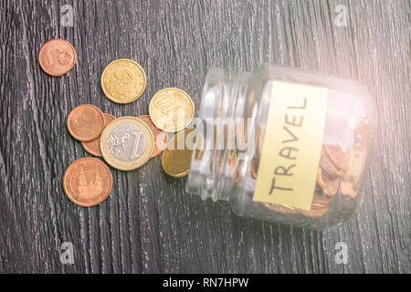 Gekippt Glas Glas mit verstreuten Münzen mit der Aufschrift auf einem schwarzen Holztisch. Das Konzept der Einsparungen für die Reisen nach Ländern und Citi Stockfoto