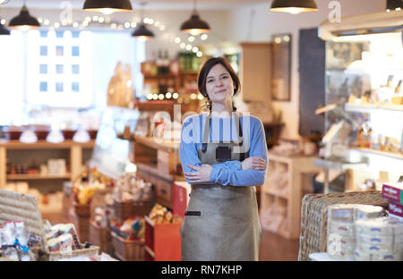 Portrait von Lächelnd weibliche Besitzer von Feinkost Shop tragen Schürze Stockfoto