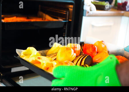 Nahaufnahme von gebratene Paprika und Auberginen in ein Fach ein Mann ist, in denen er seine Hände tragen Backofen Handschuhe. Party time Stockfoto