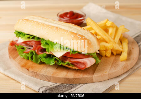 Frische submarine Sandwich mit Schinken, Käse, Speck, Tomaten und Salat auf Holz Schneidebrett mit Pommes frites und Sauce Stockfoto