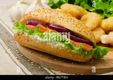 Sandwich mit Getreide, Brot, Lachs, Salat und Zwiebeln auf einem Schneidebrett Stockfoto
