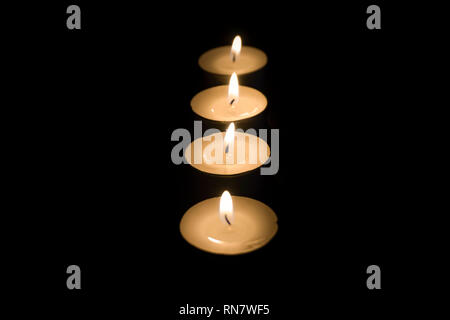 Nahaufnahme von mehreren aufgereiht Teelicht Kerzen in der Dunkelheit mit Fokus Wechsel von hinten nach vorne. Stockfoto