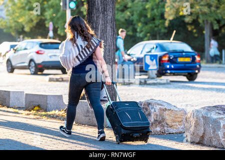 Straßburg, Elsass, Frankreich, Rückansicht einer jungen Frau, die ihren Rollenkoffer auf dem Bürgersteig zieht, Stockfoto
