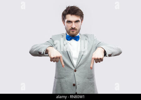 Hier und Jetzt. Porträt von Ernst herrisch aussehenden bärtigen Mann in lässigen grauen Anzug und blau Bow Tie ständigen zeigen und mit Blick auf die Pflege von Kamera. Stockfoto