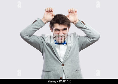 Portrait von lustig aussehenden bärtigen Mann in lässigen grauen Anzug und blauer Schleife stehen mit komischen Gesicht und Hasenohren an Kamera suchen binden. indoor Studio s Stockfoto