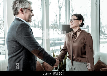 Dunkelhaarige elegante Frau in graue Hosen lächelnd zu ihr Business Partner Stockfoto